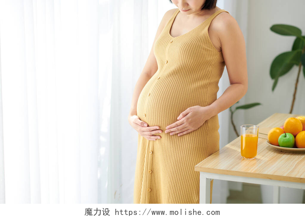一个怀孕的孕妇站在窗帘前在客厅里有健康食品的难以辨认的孕妇